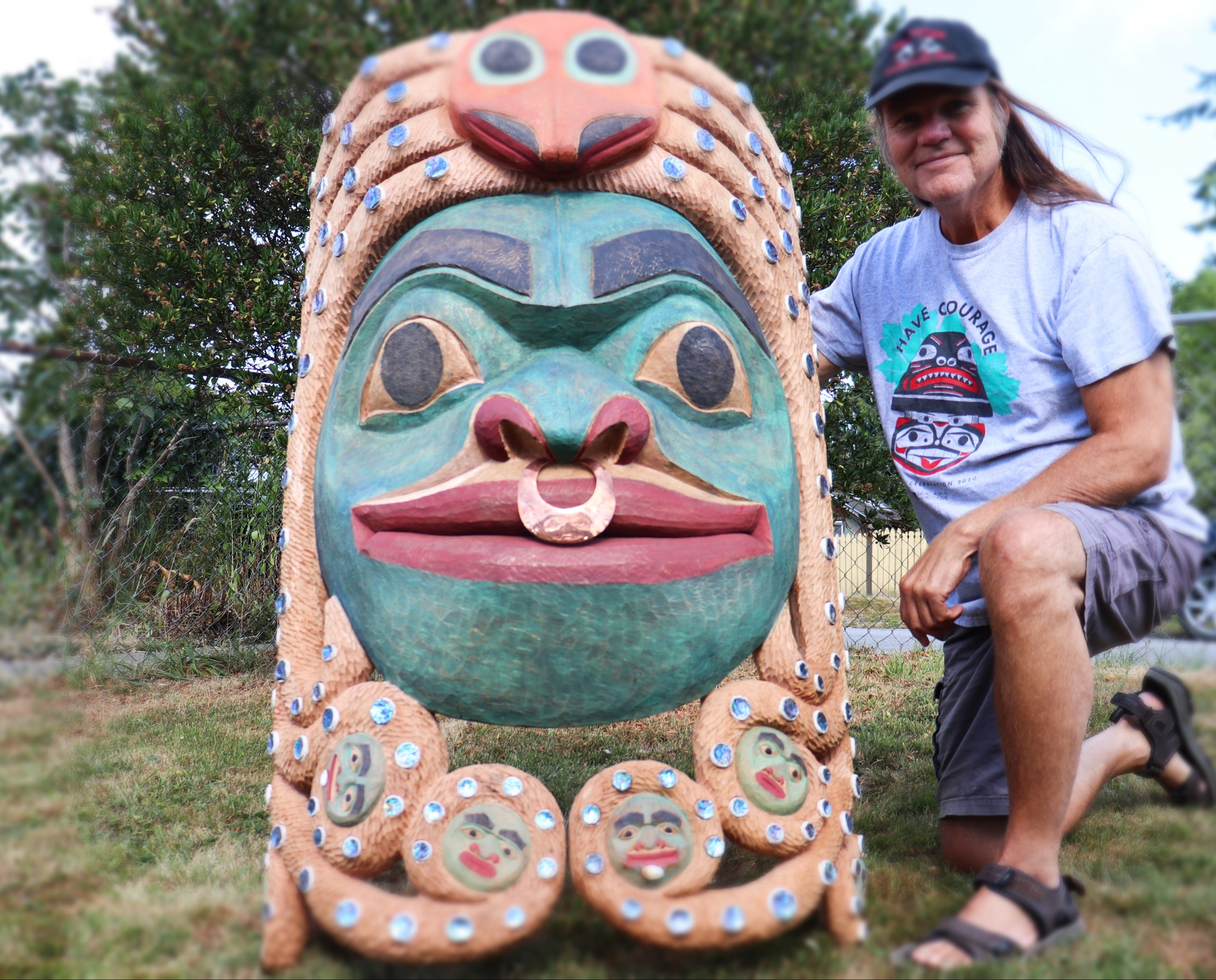 Fred Fulmer Tlingit Artist kneeling next to the finished product of the Chookaneidee Devilfish carved cedar giant mask